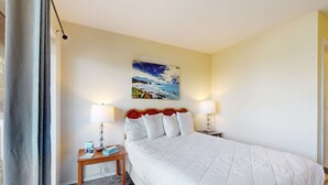 A hotel room with a large bed, two bedside tables with lamps, a painting on the wall, and a curtain on the window. - Lower Level Dog Friendly Studio with Ocean Views and Free WiFi Walk to Beach (Lincoln City)