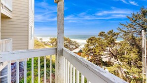 Une vue sur la côte, prise depuis un balcon doté d’une balustrade en bois, donnant sur une plage et l’océan.