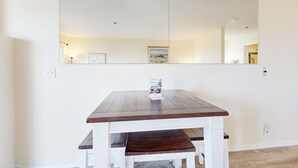 Une table à manger avec un plateau en bois foncé et un banc assorti, un grand miroir au-dessus, et un interrupteur sur le mur.