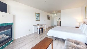 Habitación de hotel con una cama, un escritorio pequeño, una silla, un banco, chimenea y televisor montado en la pared.