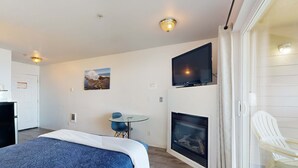 Une chambre à coucher comprenant un lit, un téléviseur fixé au mur, une cheminée et une porte vitrée donnant sur un balcon équipé d’une chaise.