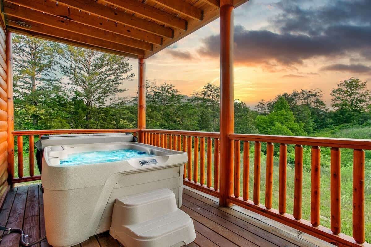 A hot tub on a wooden deck with a view of trees and a sunset.