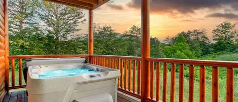 A hot tub on a wooden deck with a view of trees and a sunset.
