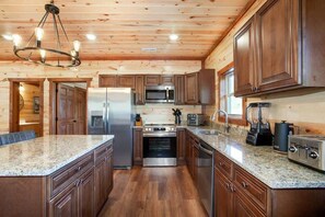A modern kitchen with wooden cabinets, stainless steel appliances, granite countertops, and a central island. - 8-Bedroom Cabin with Indoor Pool, Arcade Game Room & Hot Tub Near Dollywood (Sevierville)