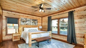 Ein Schlafzimmer einer Holzhütte mit Bett, Bank, Deckenventilator, Kunstwerken und großen Fenstern.