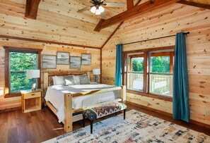 A wooden cabin bedroom with a bed, bedside tables, and a view of the outdoors. - 8-Bedroom Cabin with Indoor Pool, Arcade Game Room & Hot Tub Near Dollywood (Sevierville)