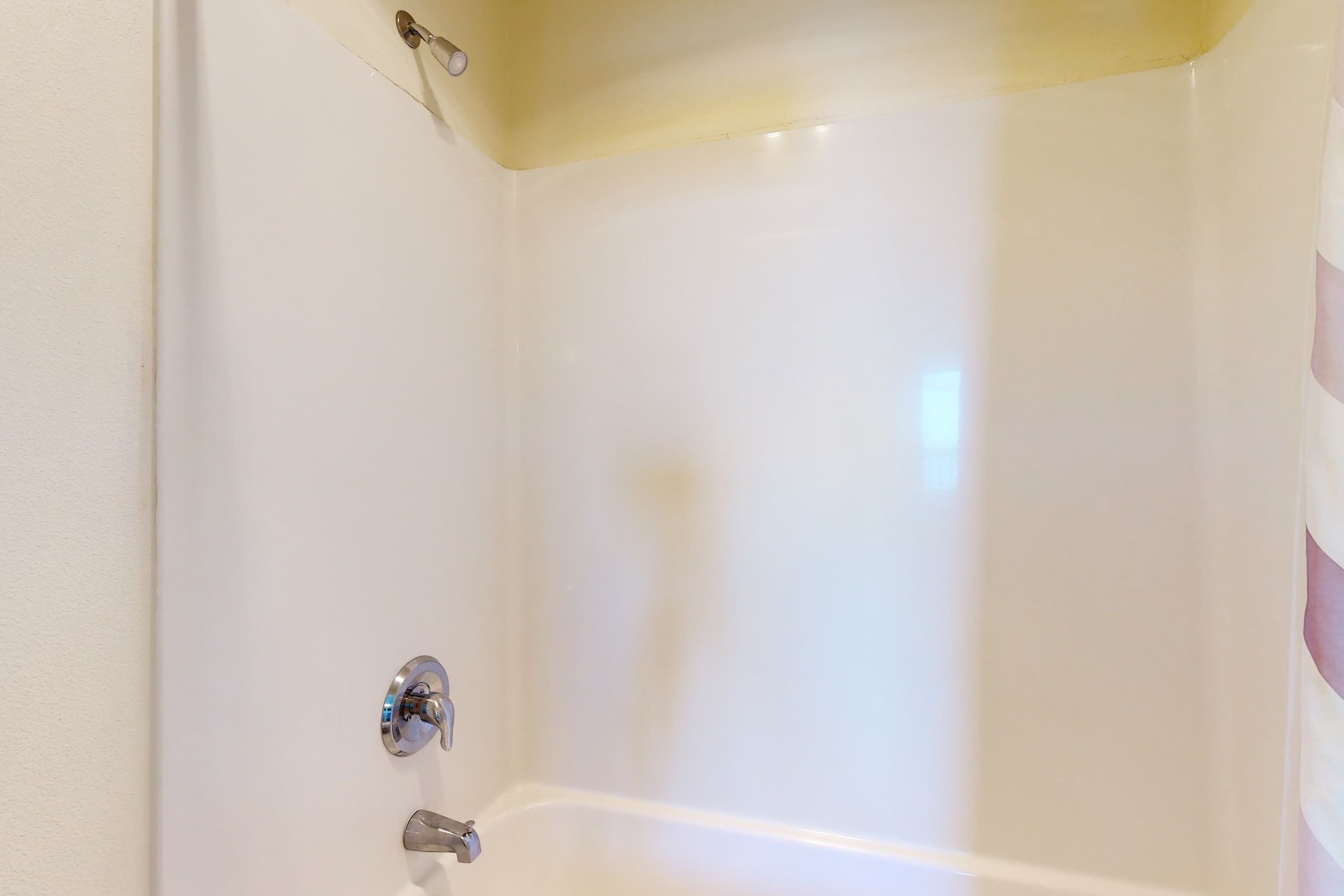 A corner of a white bathroom with a bathtub, a shower curtain rod, and a wall-mounted towel rack.