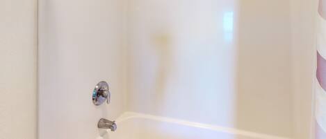 A corner of a white bathroom with a bathtub, a shower curtain rod, and a wall-mounted towel rack.