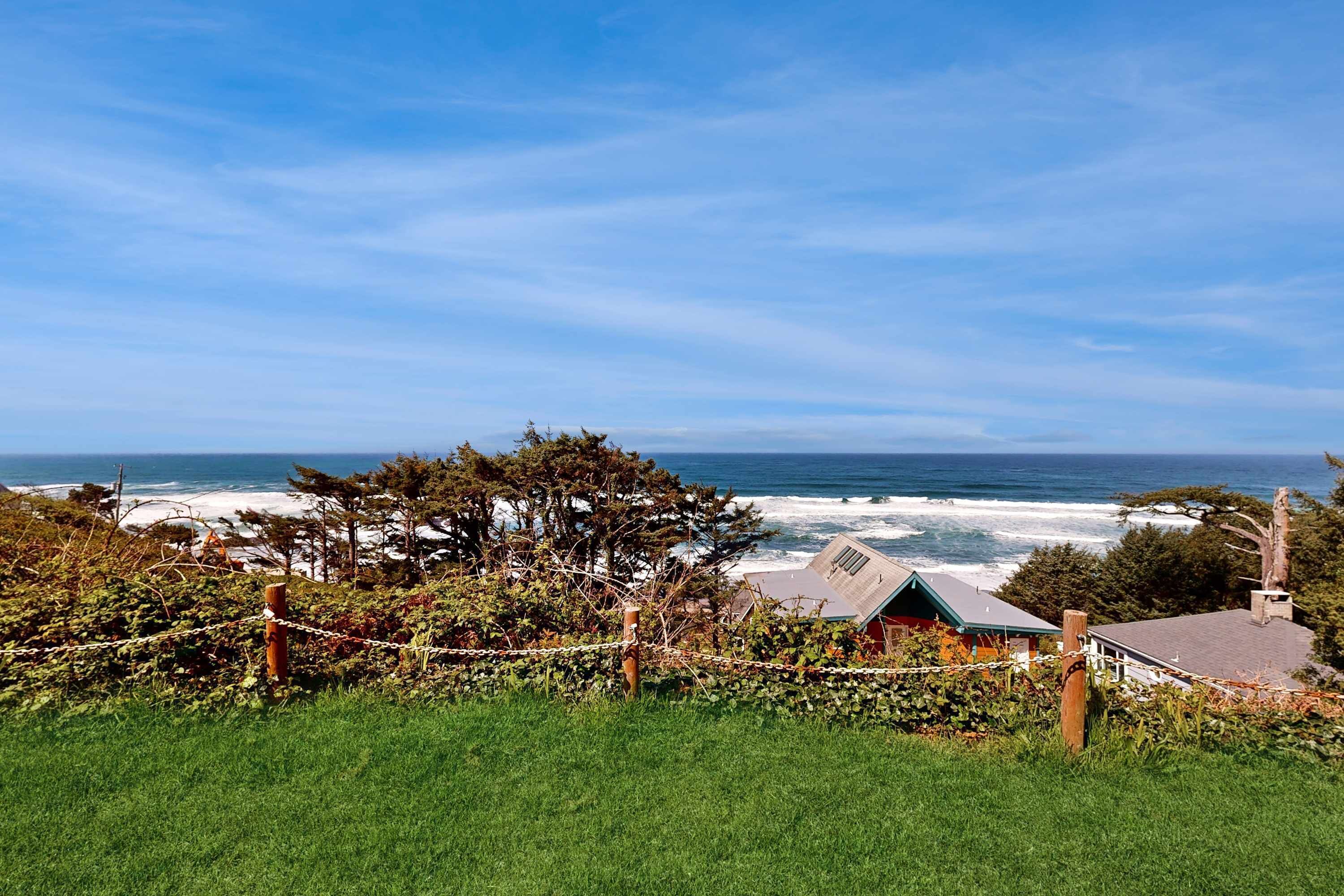 A coastal property with a view of the ocean, a fenced garden, and a house with a green roof.