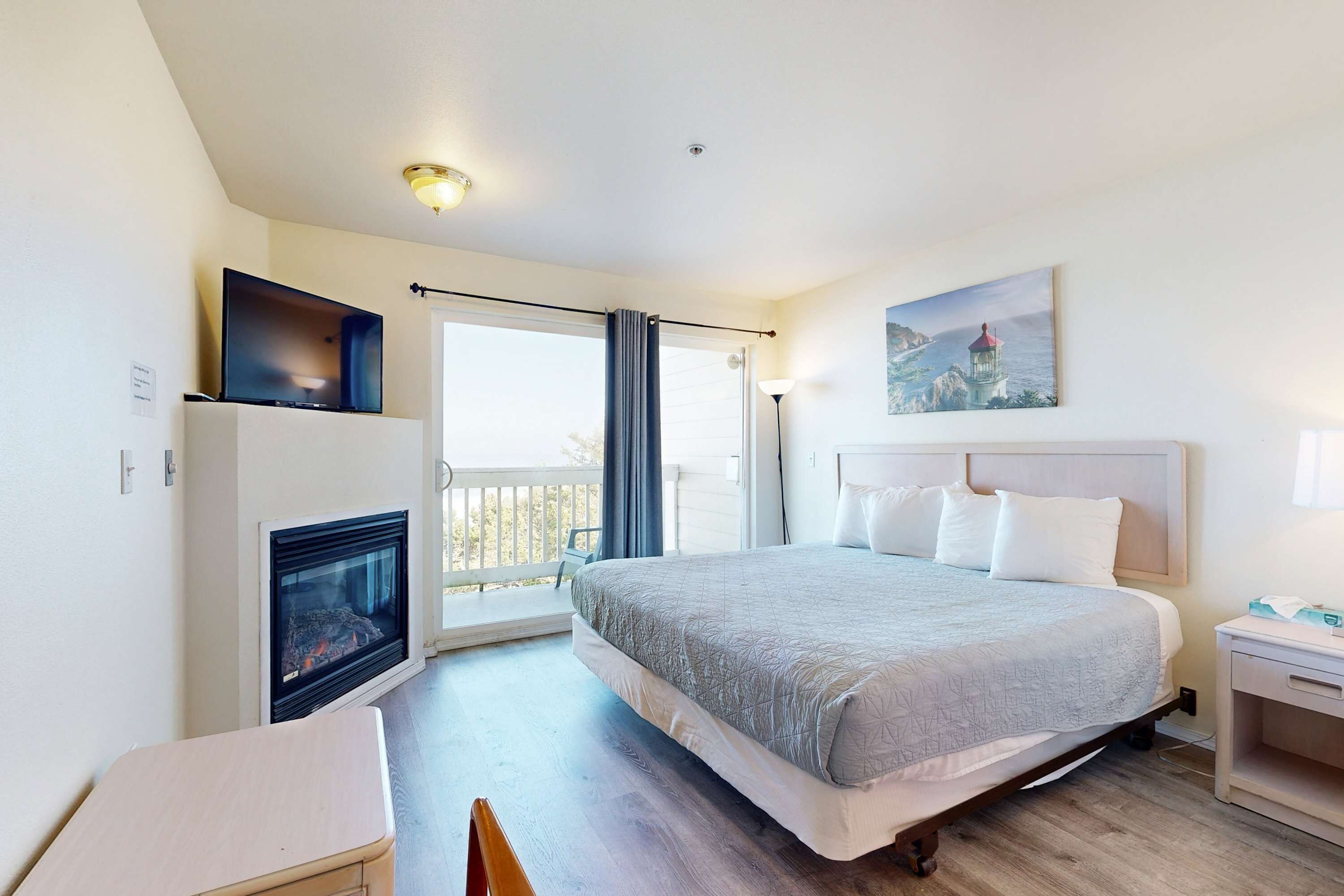 A bedroom with a bed, a fireplace, a TV, a painting, and a balcony.