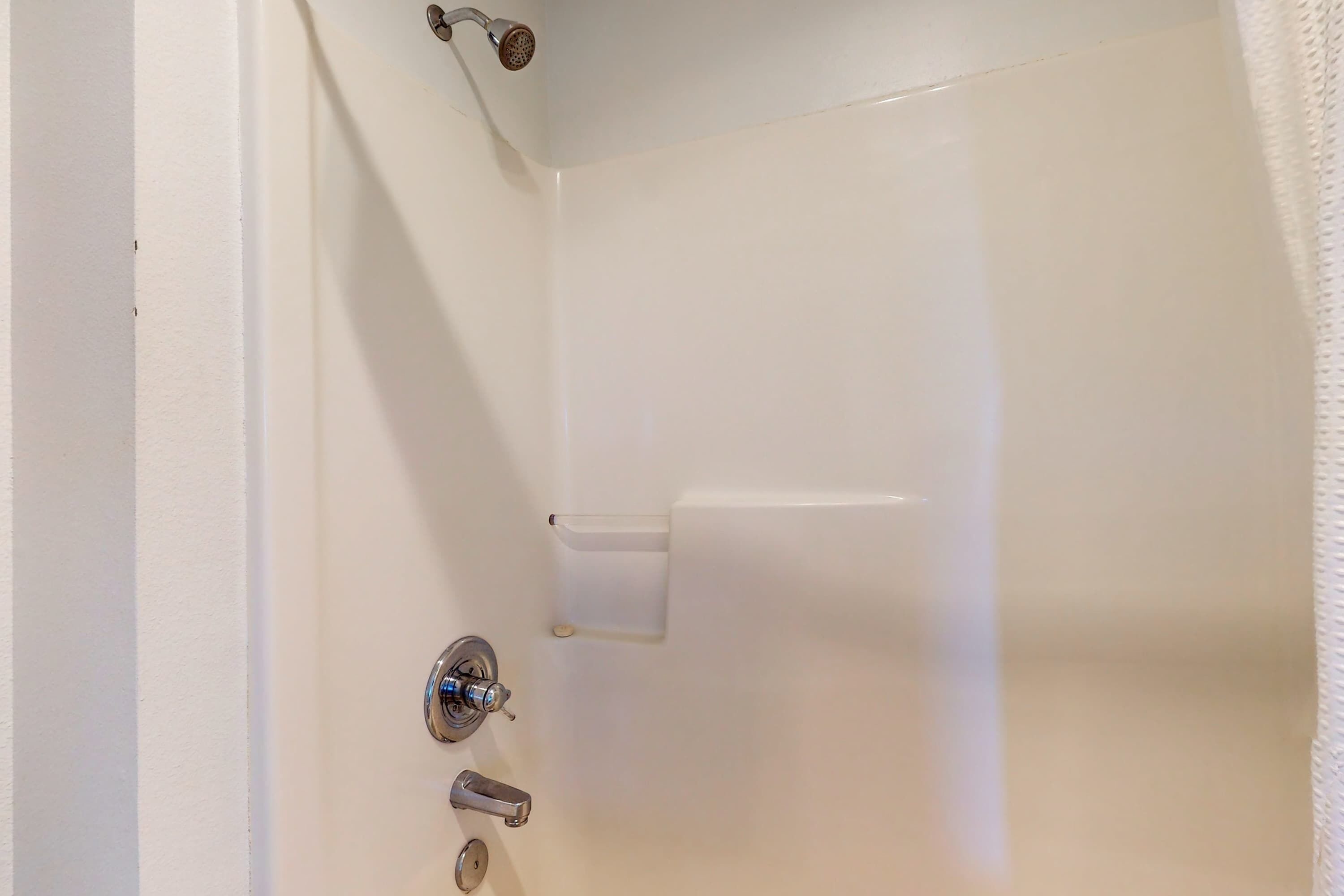 A bathroom with a white bathtub, a showerhead, a towel rack, and a toilet paper holder.