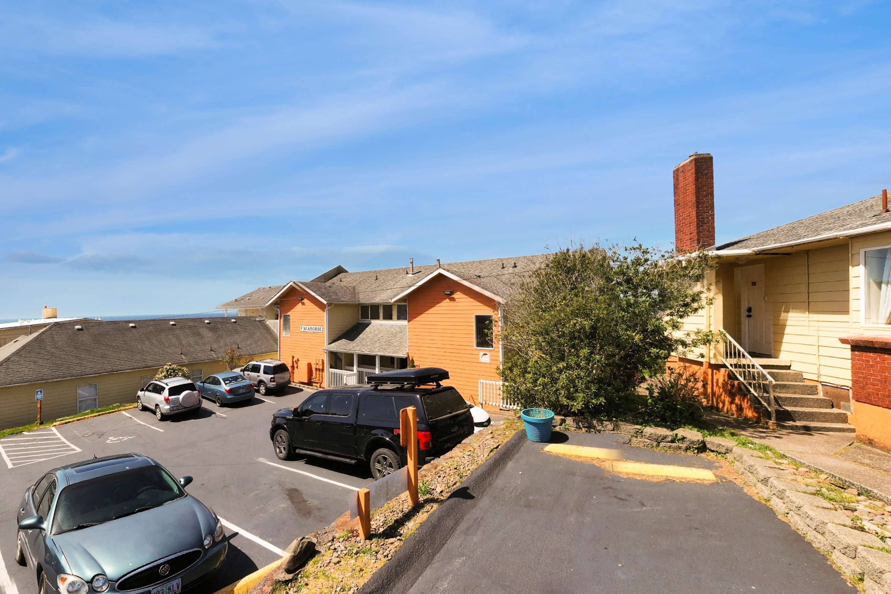 A parking lot with several cars, a building with a brick chimney, and a staircase leading to a door.