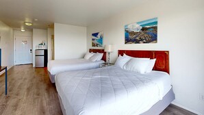 A hotel room with two beds, a desk, a refrigerator, and a painting of a coastal scene. - Oceanview Dog Friendly Studio with Awesome Views and Easy Beach Access (Lincoln City)