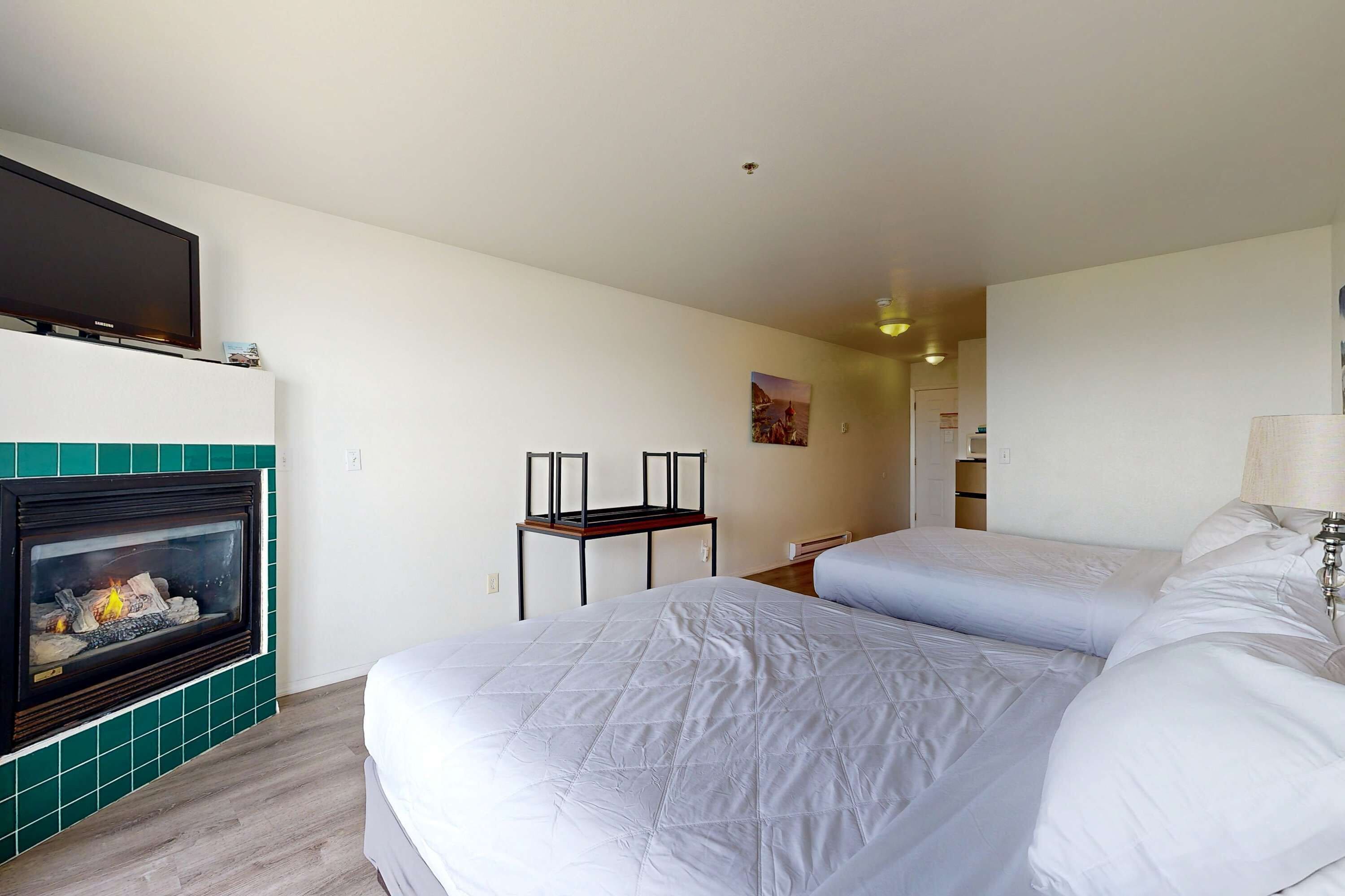 Ett hotellrum med en öppen spis, två sängar, en tv och ett litet bord.