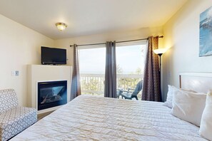 A hotel room with a bed, a TV, a fireplace, a balcony with a chair, and a painting on the wall. - Dog Friendly Suite with Ocean Views Balcony Free WiFi and Nearby Beach Access (Lincoln City)