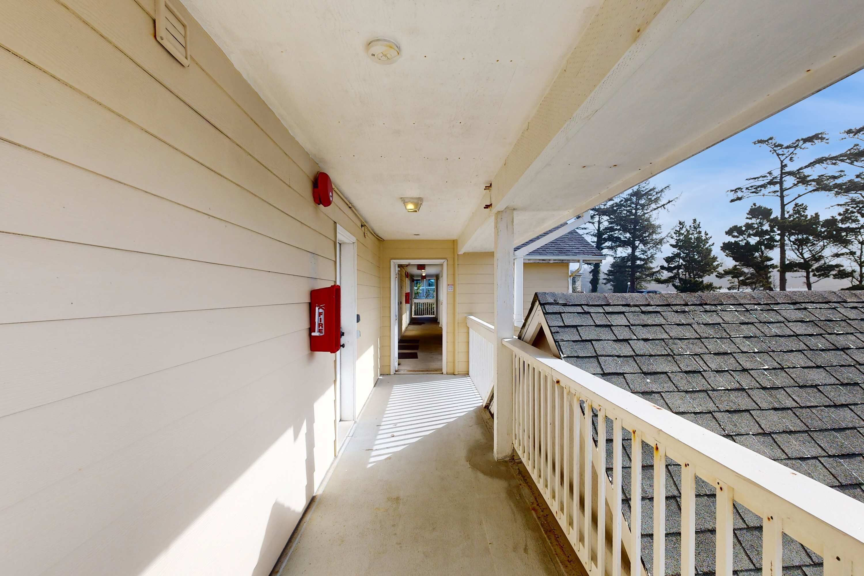 A narrow corridor with a white railing, a fire extinguisher, and a door leading to an interior space.