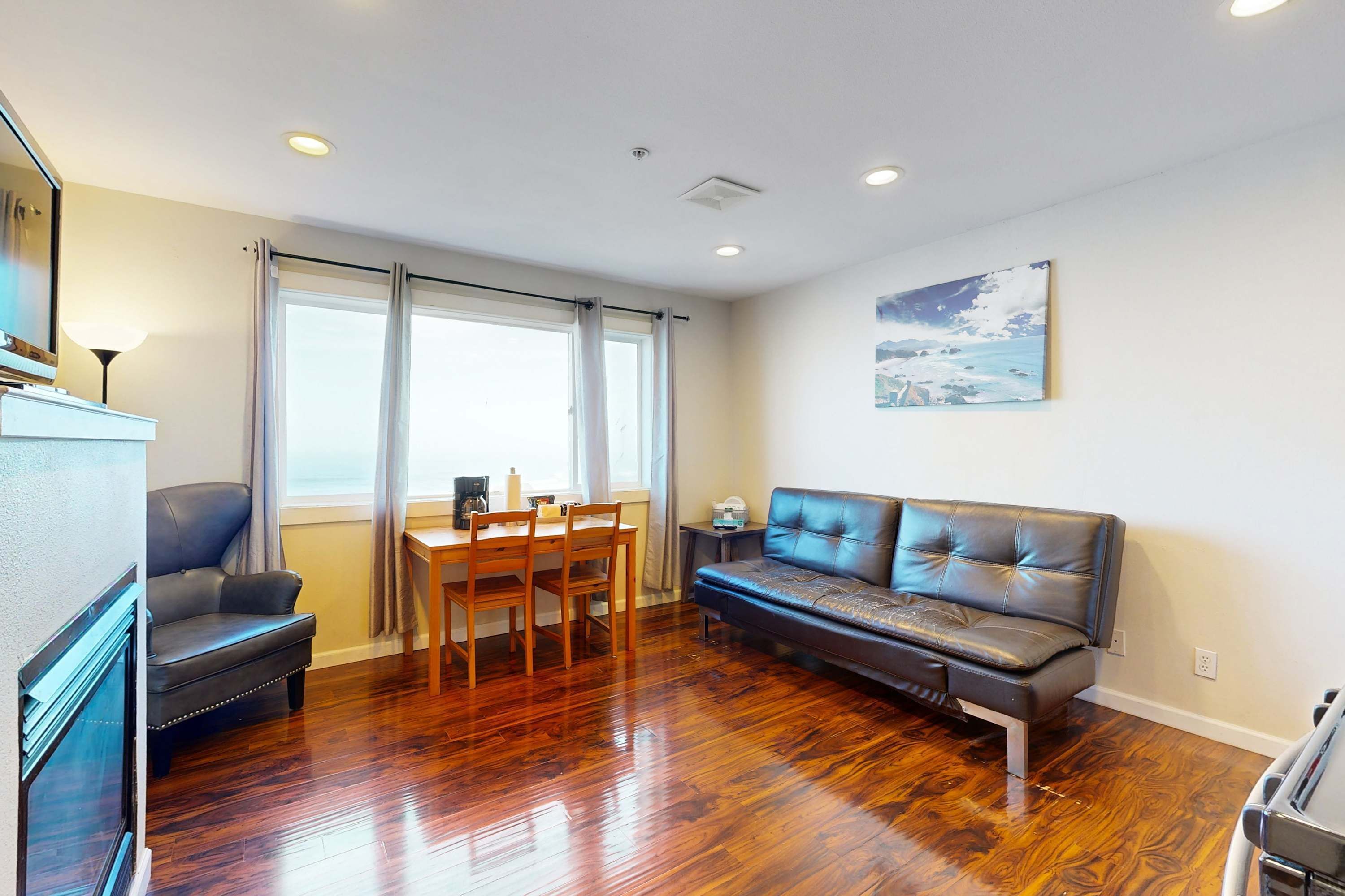 A living room with a wooden floor, a sofa, a dining table with chairs, and a fireplace.