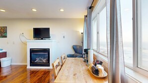 Una sala de estar moderna con chimenea, televisor, mesa de comedor y un amplio ventanal con cortinas.