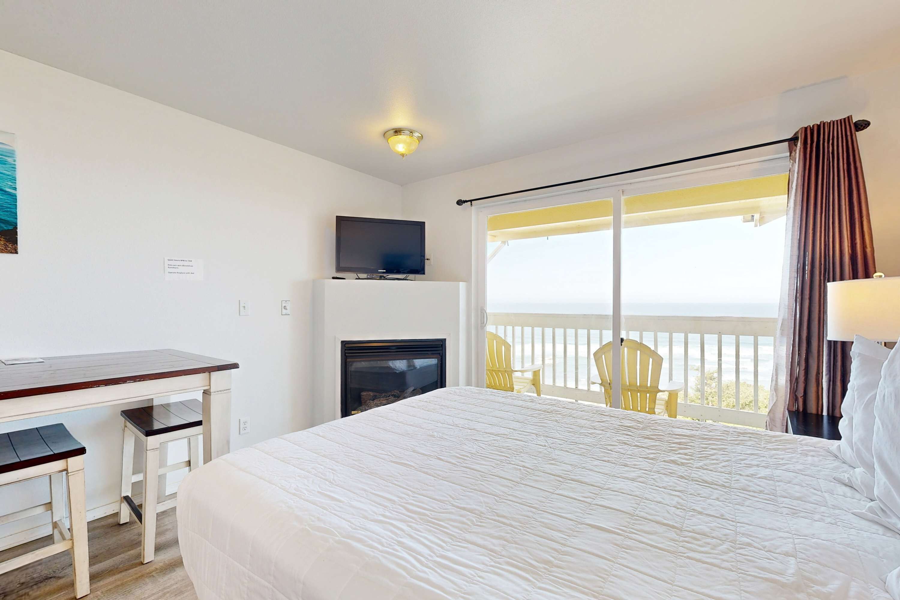 A hotel room with a bed, a desk, a television, a fireplace, and a balcony with chairs.