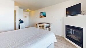 A bedroom with a bed, a television mounted on the wall, a fireplace, and a painting on the wall. - Upper Floor Oceanview Studio Perfect for Couples Free WiFi Dogs Allowed (Lincoln City)