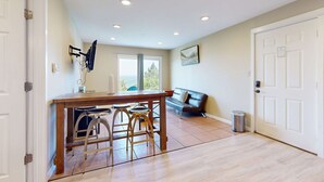 A kitchen with a wooden table and bar stools, a black couch, and a door with a sign.