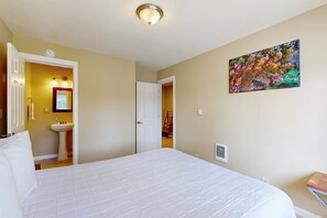 Ein Hotelzimmer mit einem großen Bett, einem Bild an der Wand, einem Waschbecken und einer Tür zu einem anderen Raum.