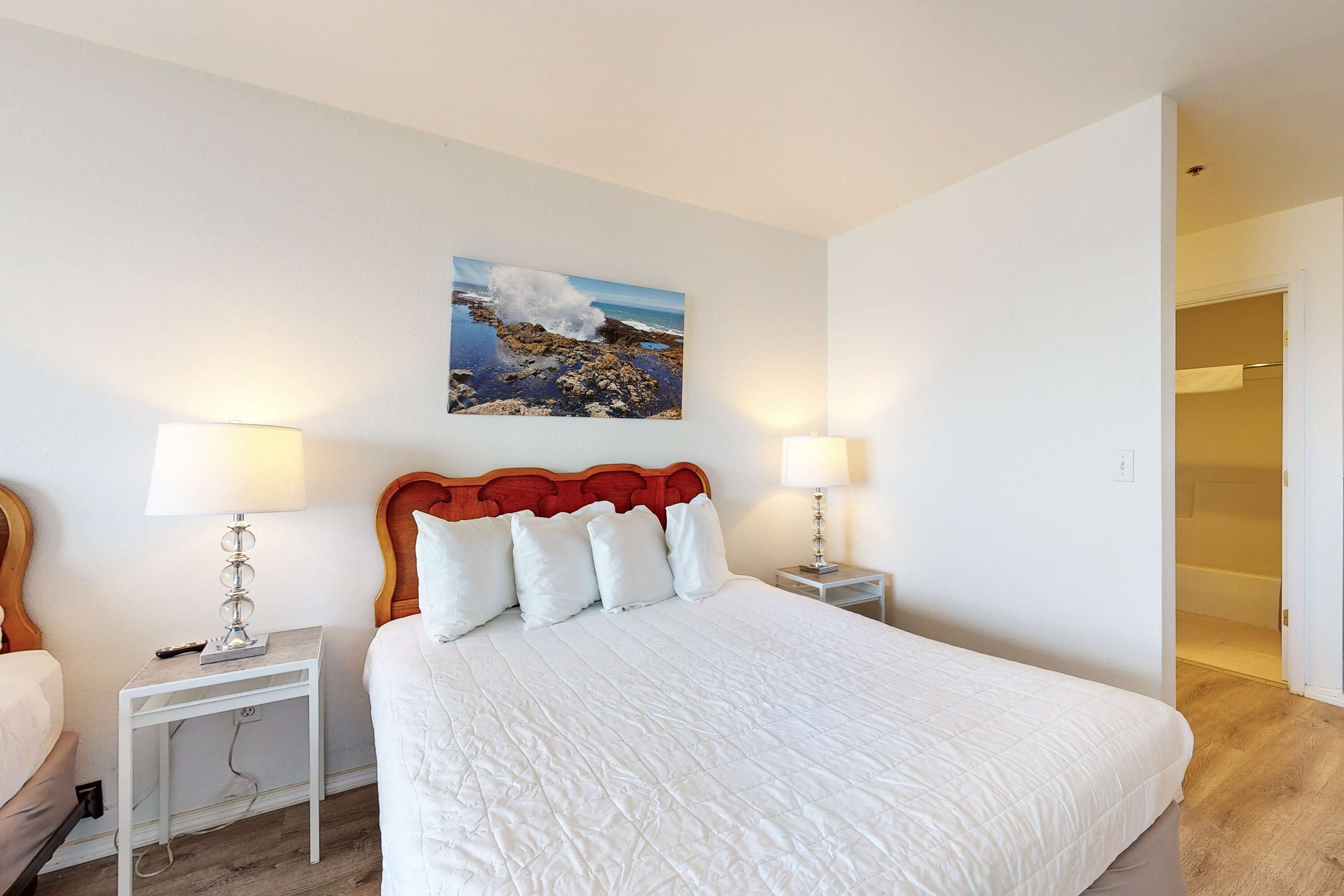 A neatly arranged bedroom with a large bed, two bedside tables with lamps, a headboard, and a wall-mounted picture.