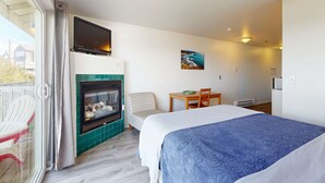 Hotellihuone, jossa on sänky, takka, televisio, ruokapöytä tuoleineen ja näkymä liukuoven kautta.