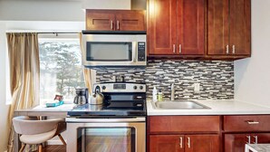 Una cucina compatta con microonde, fornello, forno e pensili in legno.