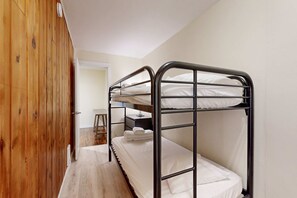 Een slaapkamer met een stapelbed, een houten garderobe en een klein tafeltje met een lamp.
