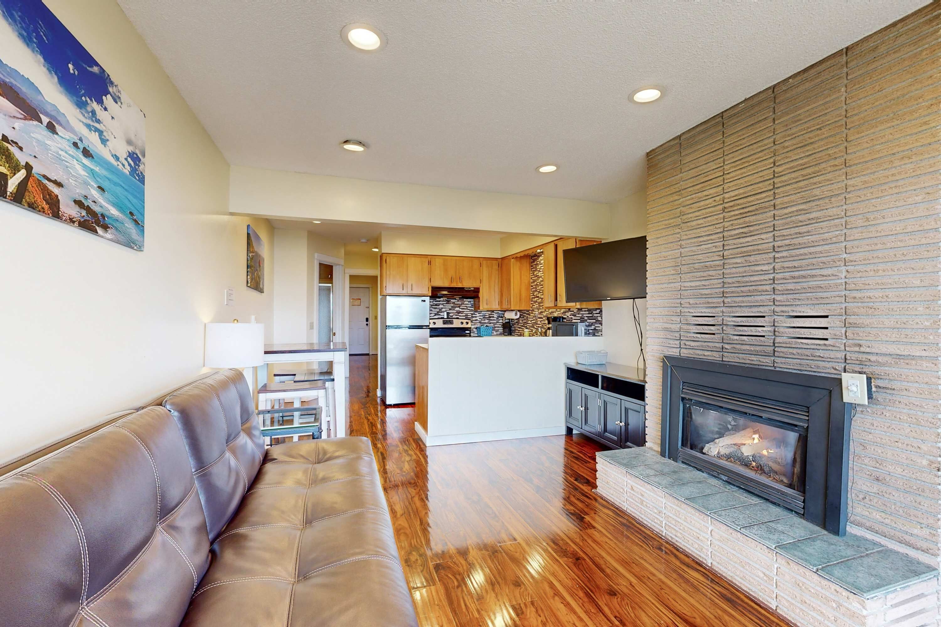 A modern living room with a leather sofa, a fireplace, and a kitchen in the background.