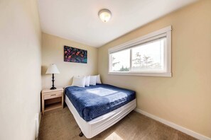 Quarto com uma cama de solteiro, mesa de cabeceira, abajur, janela com vista e luminária de teto.