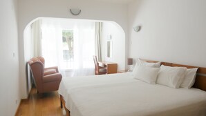 A hotel room with a large bed, a desk, a chair, and a view through a window with sheer curtains. - Dom Sancho Carvoeiro Beach Apartment Luxury (Carvoeiro)