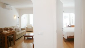 A spacious living area with a sofa, a dining table, and a chair. There is a bed in the adjacent room. - Dom Sancho Carvoeiro Beach Apartment Luxury (Carvoeiro)