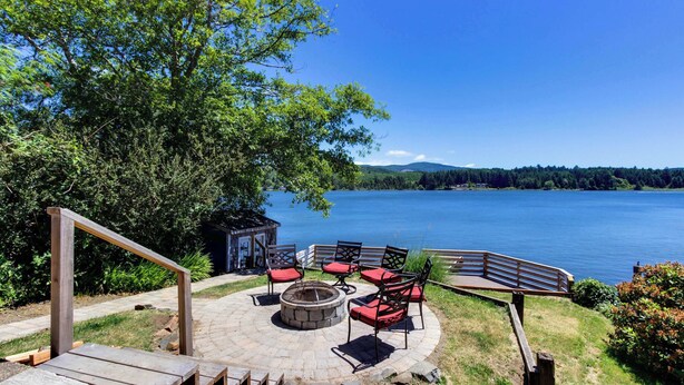 A circular outdoor seating area with a fire pit, surrounded by red cushioned chairs and a wooden bench. - Dog Friendly Lakefront Vacation Home with Stunning Views and Spacious Deck (Lincoln City)