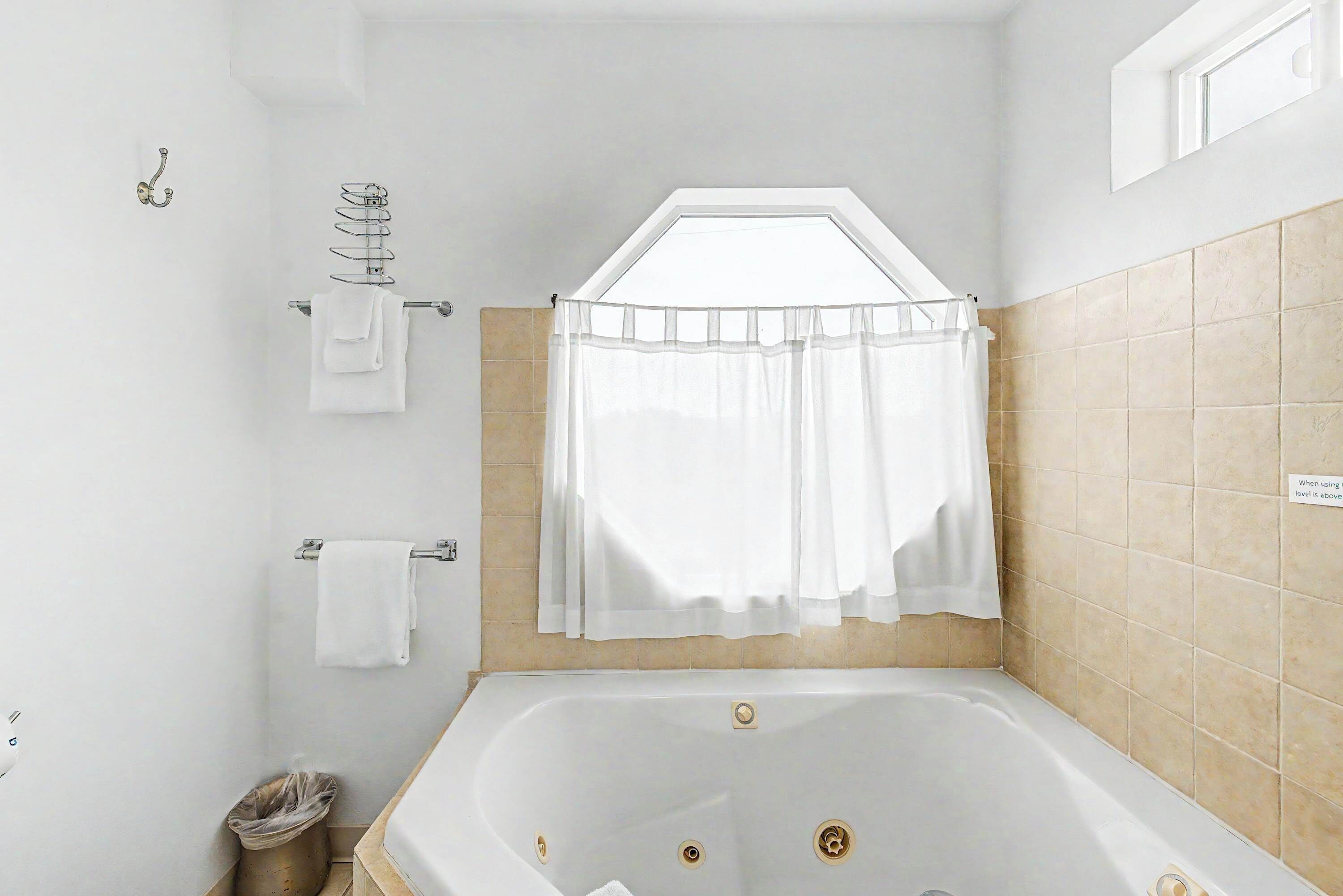 Une salle de bain avec une baignoire, un porte-serviettes, une fenêtre et un mur carrelé.