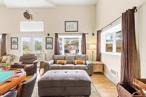 Ein Wohnzimmer mit Billardtisch, Ledersofas, einem großen Hocker und Blick ins Freie.
