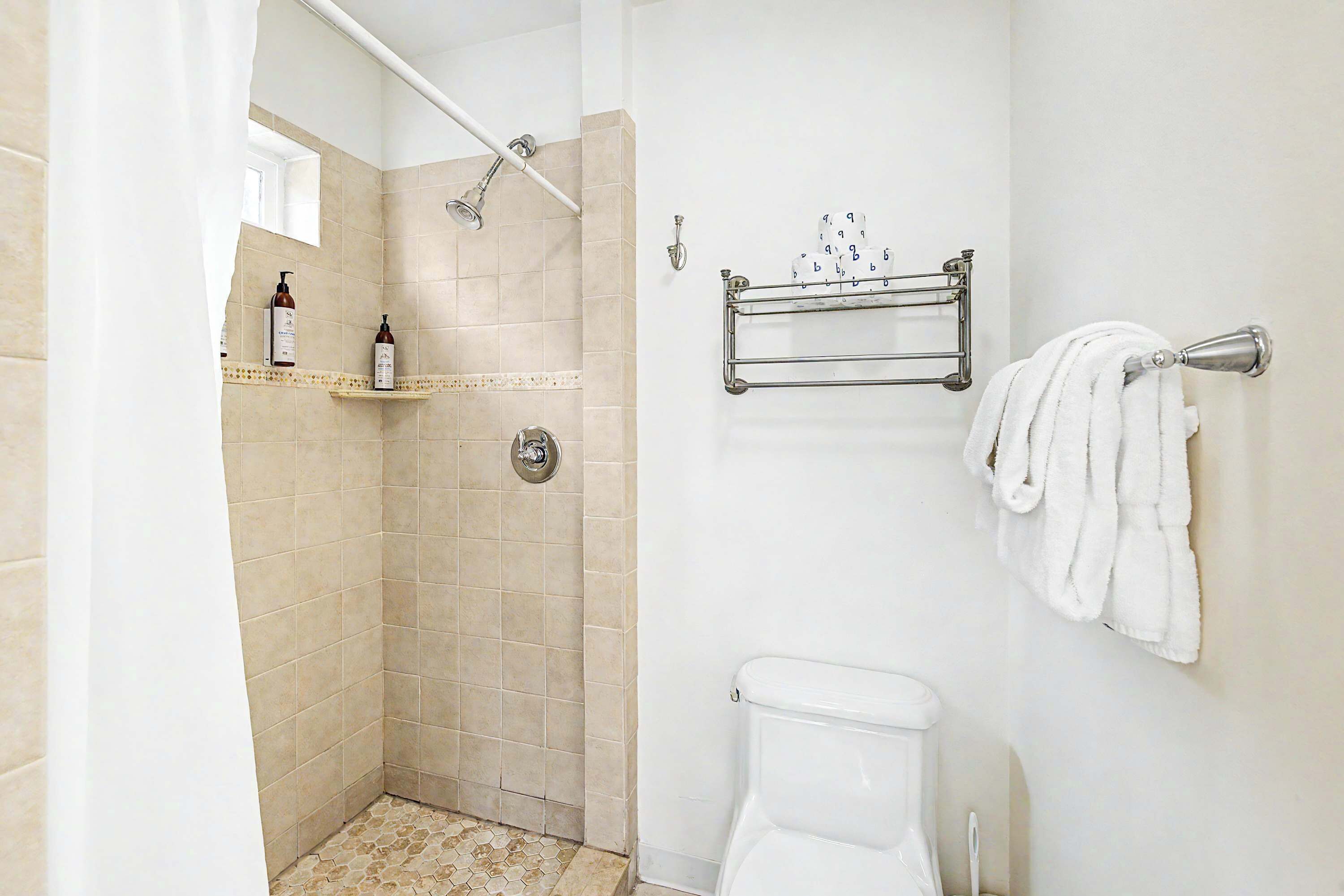 A bathroom with a shower, toilet, towel rack, and a shelf with toiletries.
