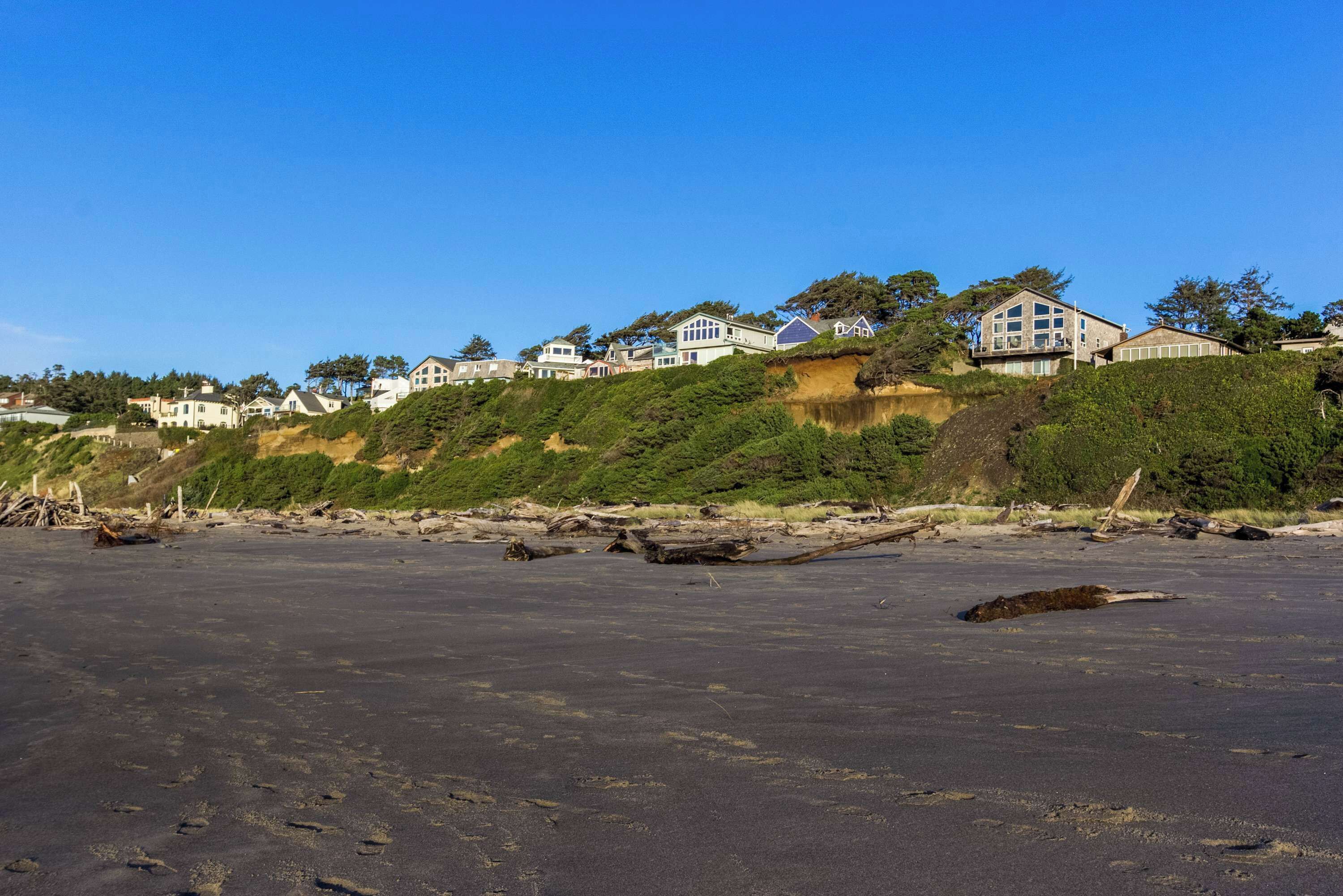 A beachfront property with multiple houses on a hillside, sandy beach in the foreground, and clear blue sky.