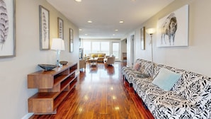A spacious living room with a wooden floor, a patterned sofa, and a dining area in the background. - Luxurious and Spacious Renovated Condo with Gorgeous Ocean Views Dogs OK (Lincoln City)