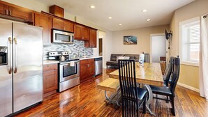 Cocina moderna con electrodomésticos de acero inoxidable, armarios de madera y una zona de comedor con mesa de madera y sillas negras.