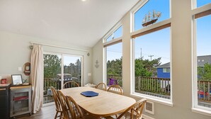 Un comedor con mesa y sillas de madera, ventanas amplias con vistas al exterior y un carrito pequeño con un marco de fotos.