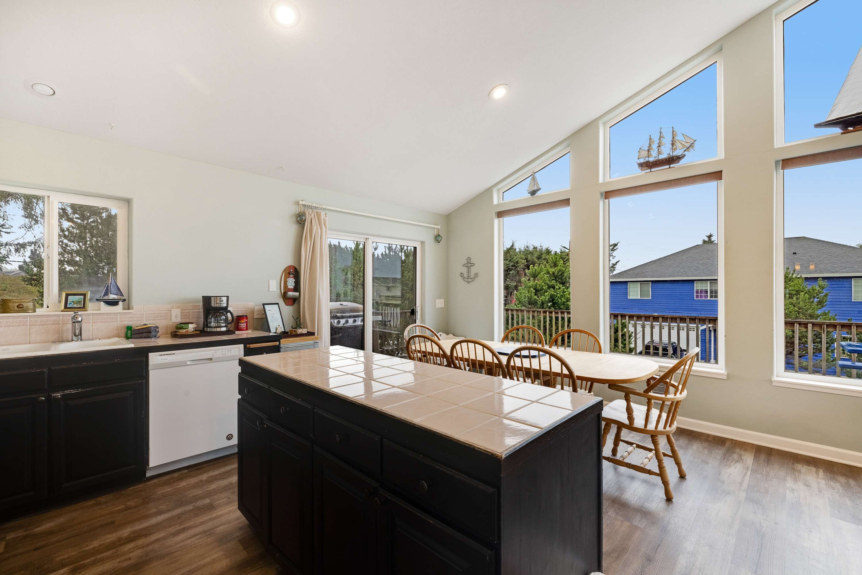 A modern kitchen with a large island, wooden dining table, and large windows offering views of the neighborhood.