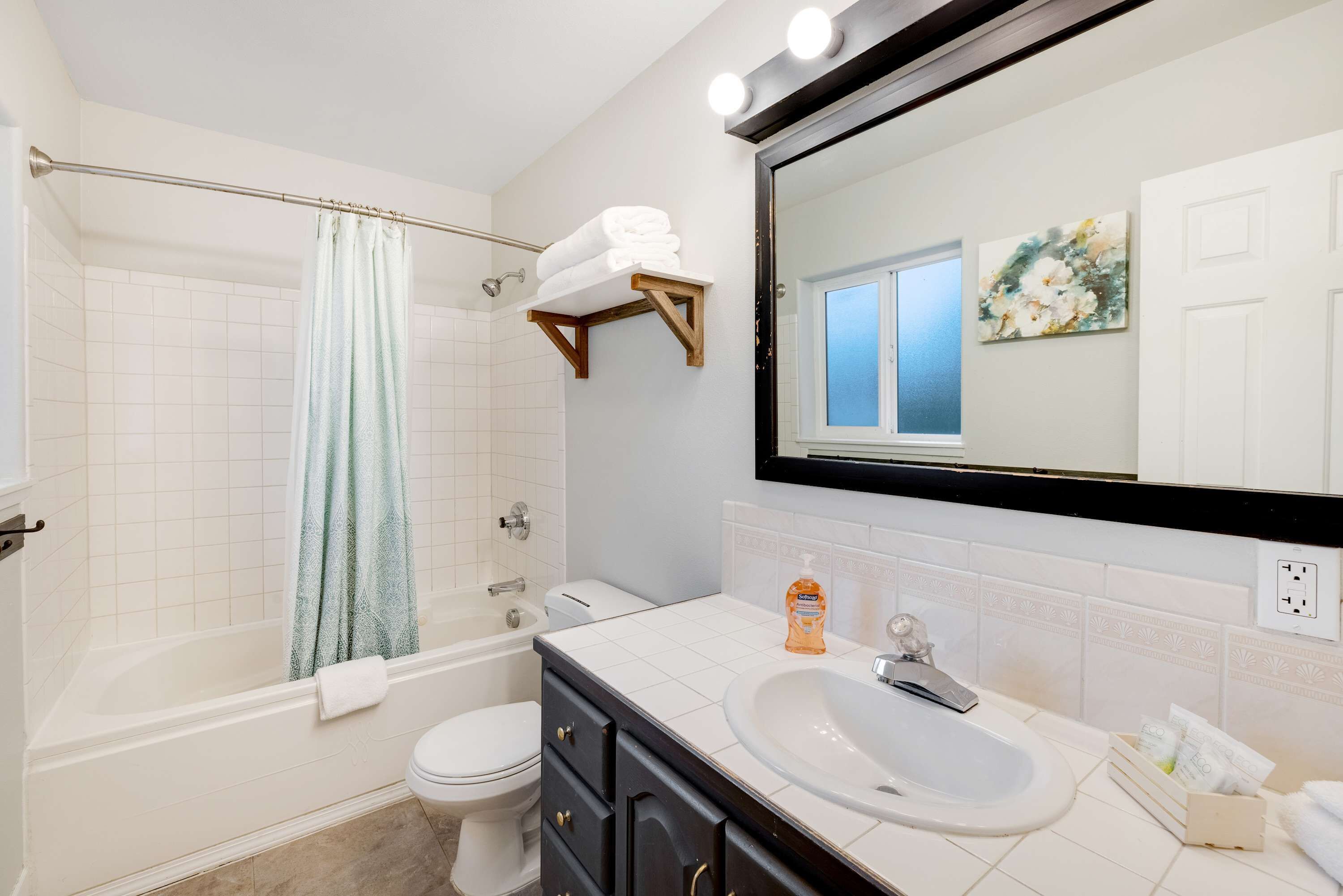 A modern bathroom with a bathtub, toilet, and sink. There is a towel rack above the sink and a mirror above the bathtub.