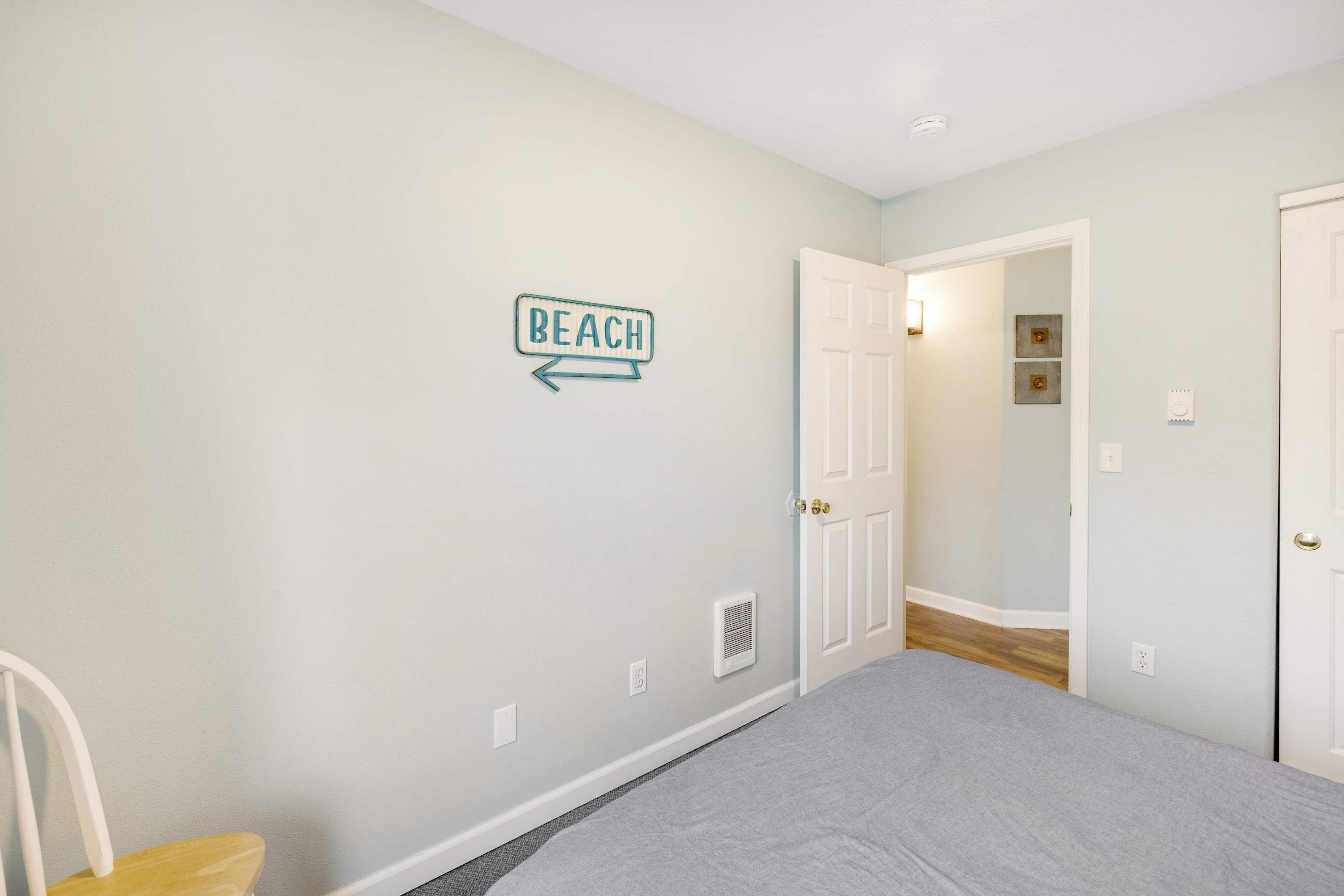 A bedroom with a bed, a chair, a door, and a wall sign that says "BEACH".