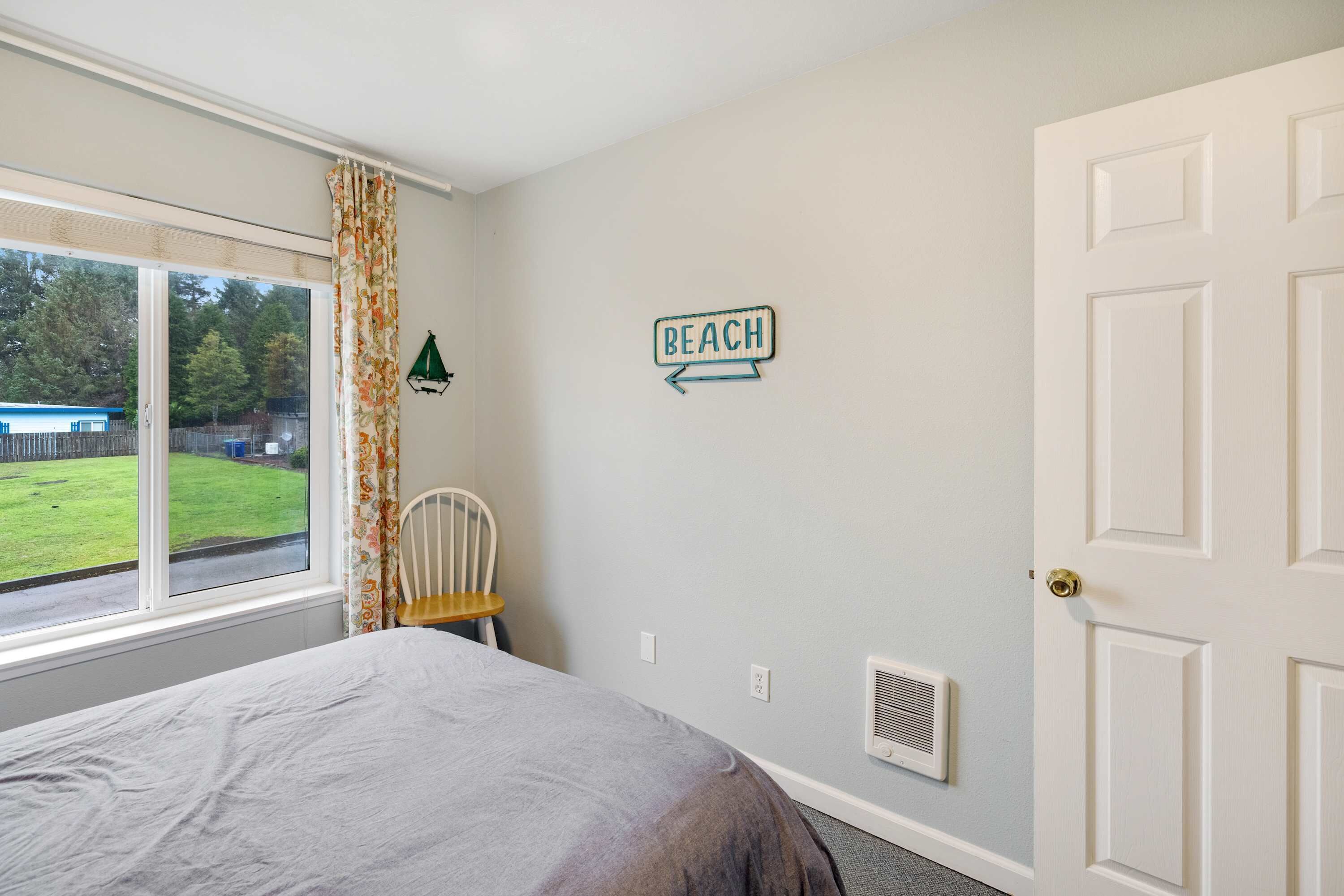 Une chambre à coucher avec un lit, une chaise, une fenêtre avec des rideaux, un panneau fixé au mur et une porte.