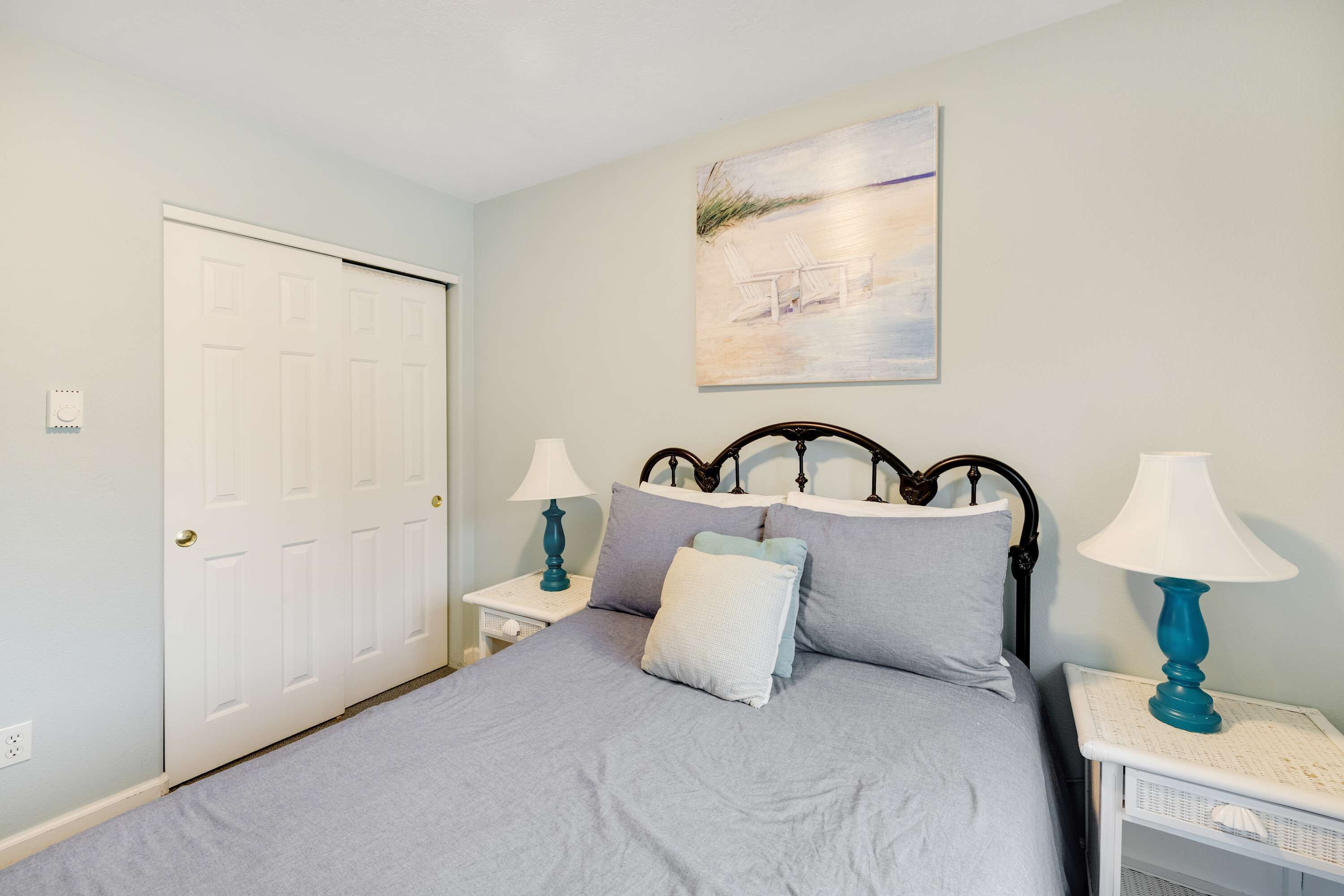 A bedroom with a bed, two bedside tables with lamps, a door, and a painting on the wall.