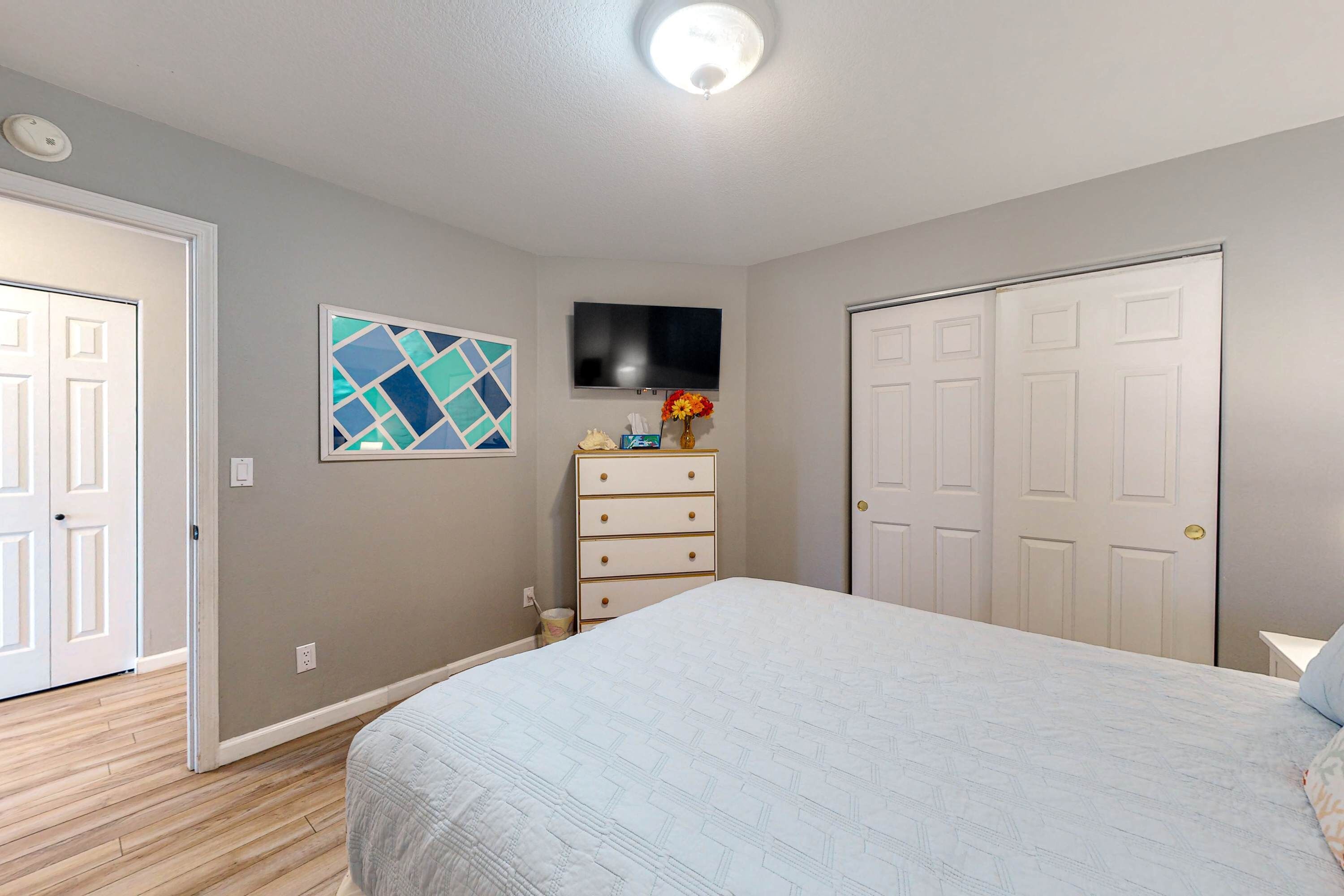 A bedroom with a bed, a dresser, a television, and a door.
