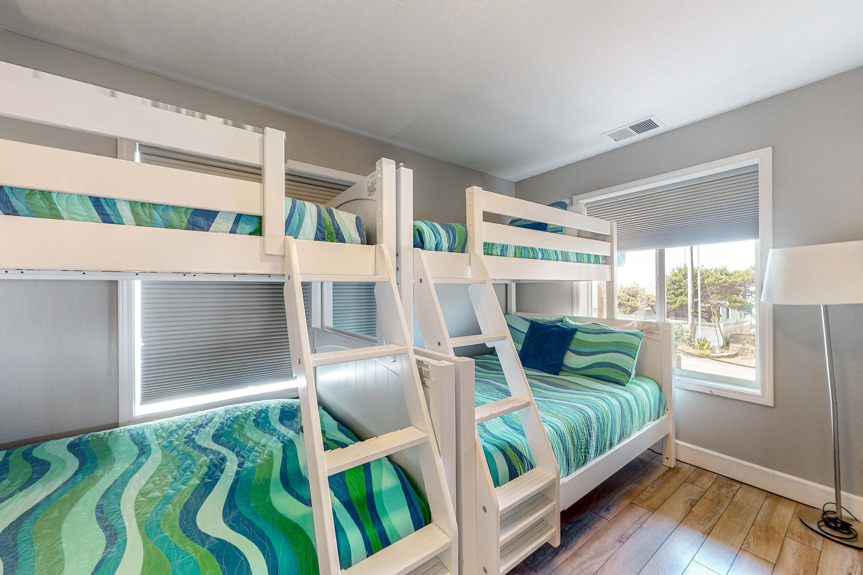 A room with bunk beds, a window with blinds, and a floor lamp.