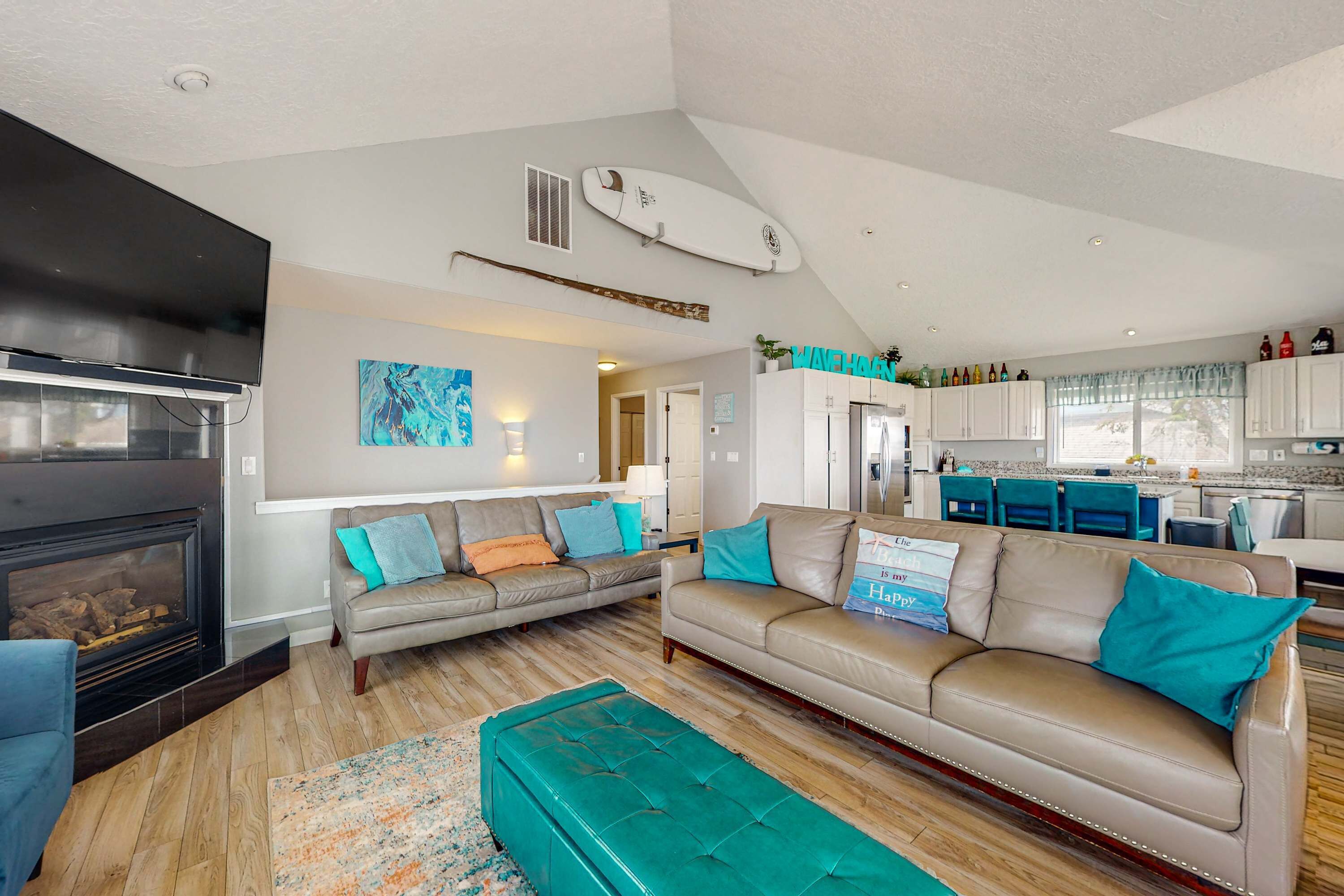 A spacious living area with a fireplace, two sofas, a large ottoman, and a kitchen in the background.
